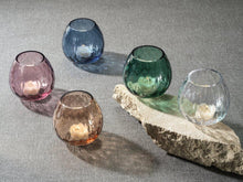 Load image into Gallery viewer, A collection of multipurpose optic vases  in various colors including green, blue, clear, brown,  and pink, with a textured design, and a rock displayed on a textured gray background.Votive candles inside each vase.