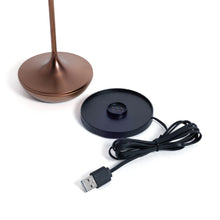 Load image into Gallery viewer, Bottom portion of the brushed copper rechargeable table light shown next to its round black magnetic charging base and USB charging cable, displayed on a white background.