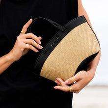 Load image into Gallery viewer, A person wearing all black holding a beige and black raffia tote bag , with white background.