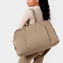 Load image into Gallery viewer, Person with long brown hair wearing a cream colored top and tan leggings, carrying a beige gym bag on shoulder. White background.