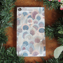 Load image into Gallery viewer, Pack of paper lunch size napkins featuring a snowy winter forest design with deer, a fox, and stylized trees in shades of blue, lavender, and gray. Displayed on a wooden surface surrounded by garland and frosted red berries.