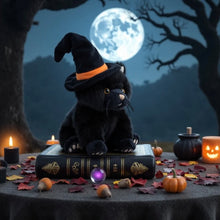 Load image into Gallery viewer, Black plush cat wearing a black witch hat with an orange band, sitting on a large closed black book. The scene is decorated with pumpkins, acorns, colorful autumn leaves, candles, and a glowing purple orb, with a full moon and silhouetted tree branches in the background.