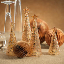 Load image into Gallery viewer, Three gold glitter cone trees with star toppers in varying heights, featuring a twinkling LED glow, displayed on a beige surface beside gold ornaments and glass decor against a warm golden background.