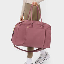 Load image into Gallery viewer, Person with a cream colored top and tan leggings carrying a mauve pink gym bag by its two handles , and  a cross body strap hanging below bag. On a white background.
