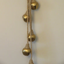 Load image into Gallery viewer, Four gold-colored metal jingle bells wrapped in jute twine, hanging in staggered lengths against a cream background.