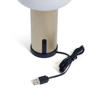 Load image into Gallery viewer, Close-view of the bottom of the textured gold-finish rechargeable table lamp on its round black charging base, connected to a USB charing cable, shown on a white background.