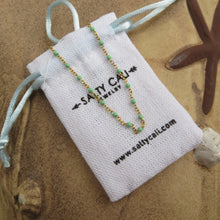 Load image into Gallery viewer, Gold chain necklace with aqua beads on a white drawstring bag with "Sally Cali" branding.