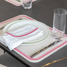 Load image into Gallery viewer, Place setting with pink embroidered lines placemat and matching napkin, 2 white plates , a glass, and silverware on a gray tabletop.