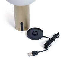 Load image into Gallery viewer, Detail of the gold-finish textured base of the rechargeable table lamp beside a round black magnetic charging base and USB cable on a white background.