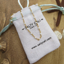 Load image into Gallery viewer, Gold necklace with white beads on a "Salty Cali" branded jewelry pouch with beach-themed background