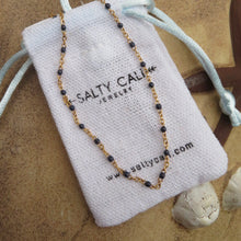 Load image into Gallery viewer, Gold chain necklace with dark blue beads on a 'Salty Cali Jewelry' branded pouch.