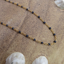 Load image into Gallery viewer, Gold chain necklace with dark blue beads on a beach surface