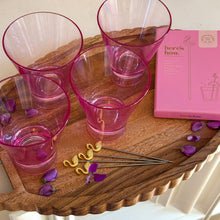 Load image into Gallery viewer, Four pink tinted glasses, a pink box of flamingo stirs, four gold flamingo picks , and purple flowers sprinkled  on a wooden tray.