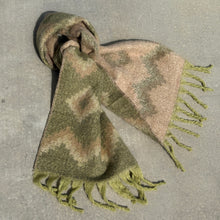 Load image into Gallery viewer, Oversized reversible knit scarf tied in a loose knot, displaying an olive side with cream and tan zigzag and diamond patterns and a cream side with olive and brown zigzag and diamond patterns, finished with light green fringe, displayed on a gray textured surface.
