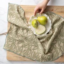 Load image into Gallery viewer, Block print napkin with a leafy pattern and green stitched edges styled on a wooden board. 