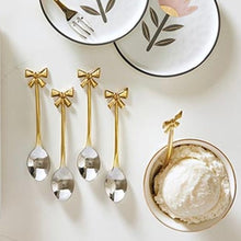 Load image into Gallery viewer, Five gold-tone bow handle spoons with silver-tone bowls displayed on a light surface, one shown in a bowl of ice cream. 