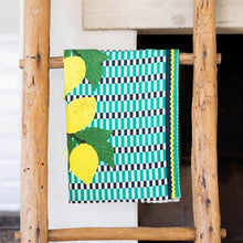 Load image into Gallery viewer, Kitchen Tea Towel, kitchen tea towel with yellow lemon illustrations, dark green leaves, teal, black, and white checkered background, teal and black border accents, and yellow rickrack trim, displayed hanging on a rustic wooden ladder against a white background.