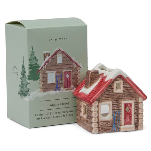 Ceramic alpine chalet candle and incense holder with a red roof, snow-dusted details, and log cabin design. Shown beside its matching green Paddywax box labeled 