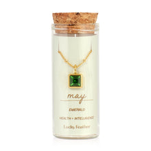 Load image into Gallery viewer, May birthstone necklace featuring a square emerald-green glass crystal pendant framed in 14K gold-dipped metal, displayed inside a clear glass bottle with cork lid and a label card reading "May - Emerald - Health + Intelligence," displayed against a white background.  