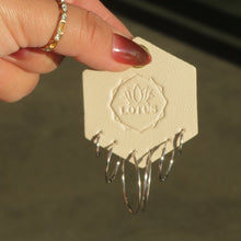 Load image into Gallery viewer, Silver-tone hoop earring set in multiple sizes displayed on a cream LOTUS card held against a textured tan surface. 