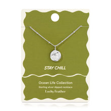 Load image into Gallery viewer, Sterling silver-dipped necklace featuring a small sea turtle charm pendant and chain with delicate beaded accents, displayed on an olive green &quot;Stay Chill&quot; Ocean Life Collection card by Lucky Feather with a white wavy border against a white background. 