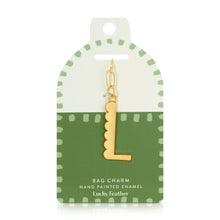 Load image into Gallery viewer, 14K gold-plated hand-painted enamel initial bag charm featuring the letter L with a scalloped edge design and a brushed gold finish, attached to a key ring and clasp. Displayed on a white and green Lucky Feather card with a light green dotted brush-stroke borders labeled &quot;Bag Charm Hand Painted Enamel.&quot; Displayed against a white background. 