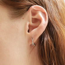Load image into Gallery viewer, Close-up of a model's ear wearing a sterling silver huggie earring featuring an X-shaped, crystal-accented crossover design.