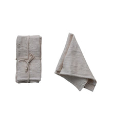 Load image into Gallery viewer, A set of folded white cotton waffle napkins ,wrapped with a white  ribbon . Next to an identical white unfolded napkin. On a white background.  