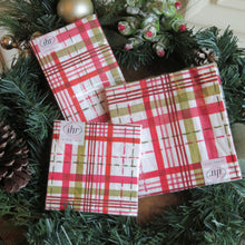 Load image into Gallery viewer, Three &quot;Merry Berry Plaid&quot; paper napkin packs in red, pink, green, and white plaid, surrounded by garland, pinecones, and frosted berries.   