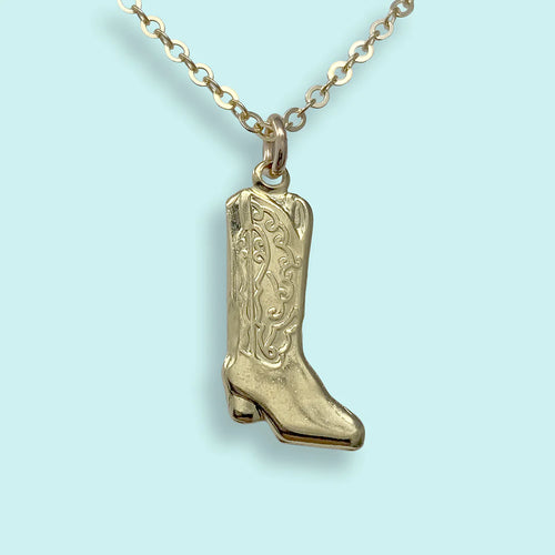 Small gold charm in the shape of cowboy boot on a gold chain. Light blue background. 