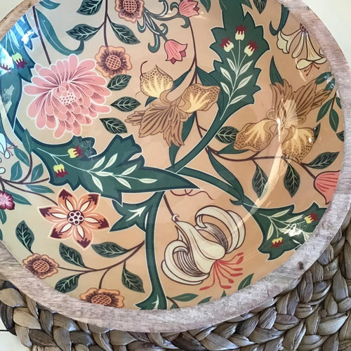 Decorative enamel bowl with a pink, white,  tan, and  green floral design on a woven surface.