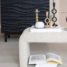 Load image into Gallery viewer, Decorative white  table with various candlesticks and books with black armoire in background.