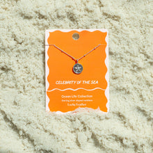 Load image into Gallery viewer, Sterling silver-dipped necklace featuring a small starfish charm pendant and a chain with delicate beaded accents, displayed on an orange &quot;Celebrity of the Sea&quot; Ocean Life Collection card by Lucky Feather with a white wavy border, shown resting on white textured sand. 