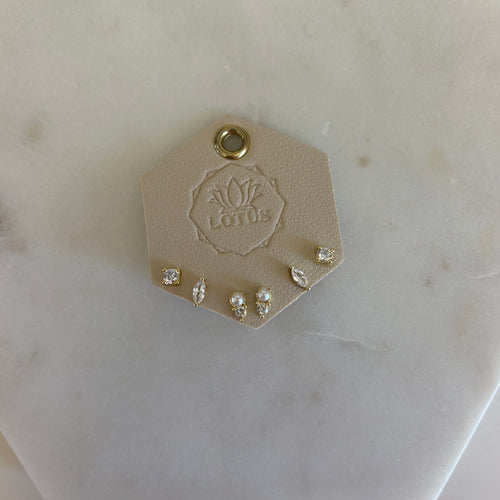 Three pairs of diamond studs fixed to a piece of faux leather. One pair is square cut, one diamond cut, and one triangle cut with a small white pearl. Flat laid on a white marble background. 