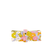 Load image into Gallery viewer, Floral makeup brush roll folded and secured with a matching strap, featuring a mustard yellow, pink, orange, lavender, and white retro flower pattern, displayed on a black and gray checkered background. 