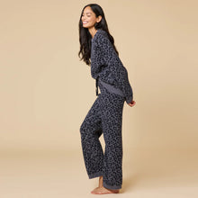 Load image into Gallery viewer, Person smiling and posing in a soft gray lounge set with a black leopard print pattern. The relaxed-fit sweater and drawstring wide-leg pants feature gray ribbed cuffs and hems, shown against a soft beige background. 