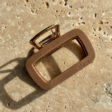 Load image into Gallery viewer, Tan rectangular metal claw clip with gold hardware displayed on a beige travertine surface with soft shadows. 