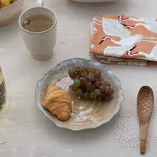 Load image into Gallery viewer, White bowl with a croissant and grapes on a white table top with a teacup, a folded crane patterned napkin and a wooden fish spoon.