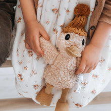 Load image into Gallery viewer, Child wearing a white dress with a pink flower design holding a cream-colored duck plushie featuring a textured curly body, light brown corduroy beak and feet, and a tan knit hat.