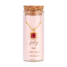 Load image into Gallery viewer, July birthstone necklace featuring a square ruby-red glass crystal pendant framed in 14K gold-dipped metal, displayed inside a clear glass bottle with a cork lid and a label card reading "July - Ruby - Power + Energy," displayed against a white background. 