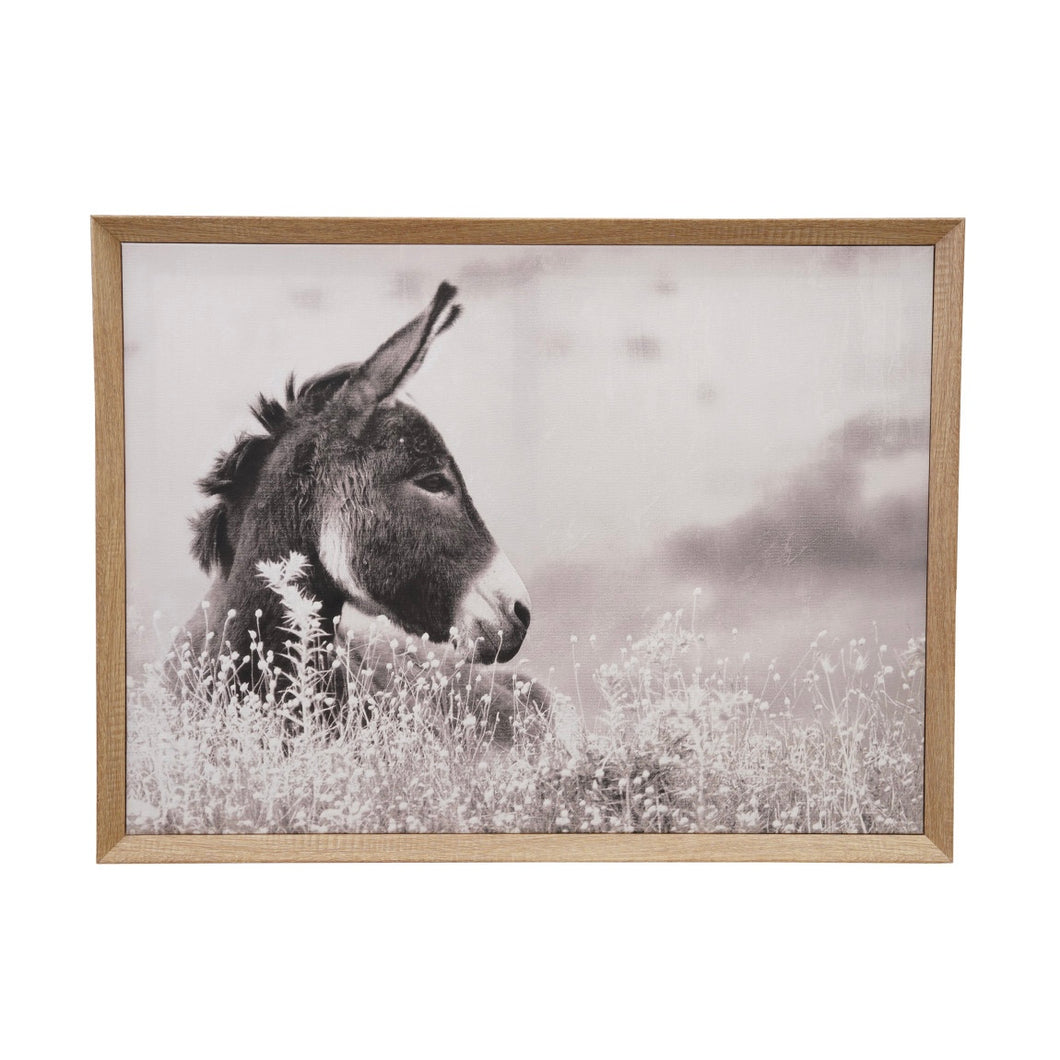 Framed artwork of a donkey in a field with a wooden frame, hanging on white wall.