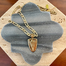 Load image into Gallery viewer, Gold paper clip chain necklace with a raised Archangel pendant, displayed on a quatrefoil-shaped gray stone tile layered over a beige travertine slab on a wooden surface.  