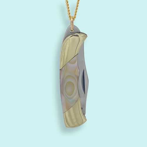 Gold and abalone pendant in the shape of a pocket knife. Light blue background. 