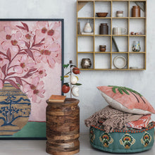 Load image into Gallery viewer, Decorative room interior consisting of a shelf with knick-knacks, a large wooden framed  floral painting, a pink pillow and  throws on a colorful ottoman, and a small circular wooden table.  