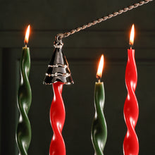 Load image into Gallery viewer, Wave tree candle snuffer in a gold finish designed with a wave-inspired pine tree shape, shown in use above lit red and green twisted taper candles against a dark background. 