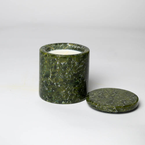 A green marble candle holder with a lid, containing a white candle, placed on a white surface.
