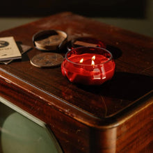 Load image into Gallery viewer, A red lit candle in a clear glass holder on a wooden table with books and coasters. Darkened background. 