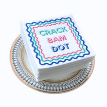 Load image into Gallery viewer, Stack of white cocktail napkins printed with the words "CRACK BAM DOT" in colorful lettering and bordered by a wavy multicolored lines, displayed on a decorative round plate with a gold and dark gray patterned border.  