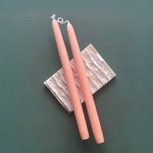 Load image into Gallery viewer, Two hand-dipped blush pink taper candles with white wicks, displayed on a textured block against a green background.