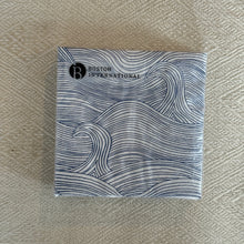 Load image into Gallery viewer, Folded paper cocktail napkins with blue wave pattern on white background, displayed on woven neutral surface.
